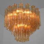 Merlande Amber Glass Tube Tiered Chandelier | Fluted Amber Glass and Brass | Full product view illuminated gracefully against a plain grey backdrop | Severn Lighting