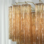 Merlande Amber Glass Tube Tiered Chandelier | Fluted Amber Glass and Brass | Side close-up view of tiered amber glass tubes against a white wall | Severn Lighting
