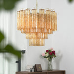 Merlande Amber Glass Tube Tiered Chandelier | Fluted Amber Glass and Brass | Real-life installation view displayed near a white wall and staircase corner | Severn Lighting