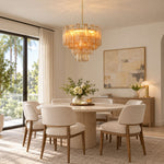 Merlande Amber Glass Tube Tiered Chandelier | Fluted Amber Glass and Brass | Positioned over a round marble dining table with cream chairs and art decor | Severn Lighting