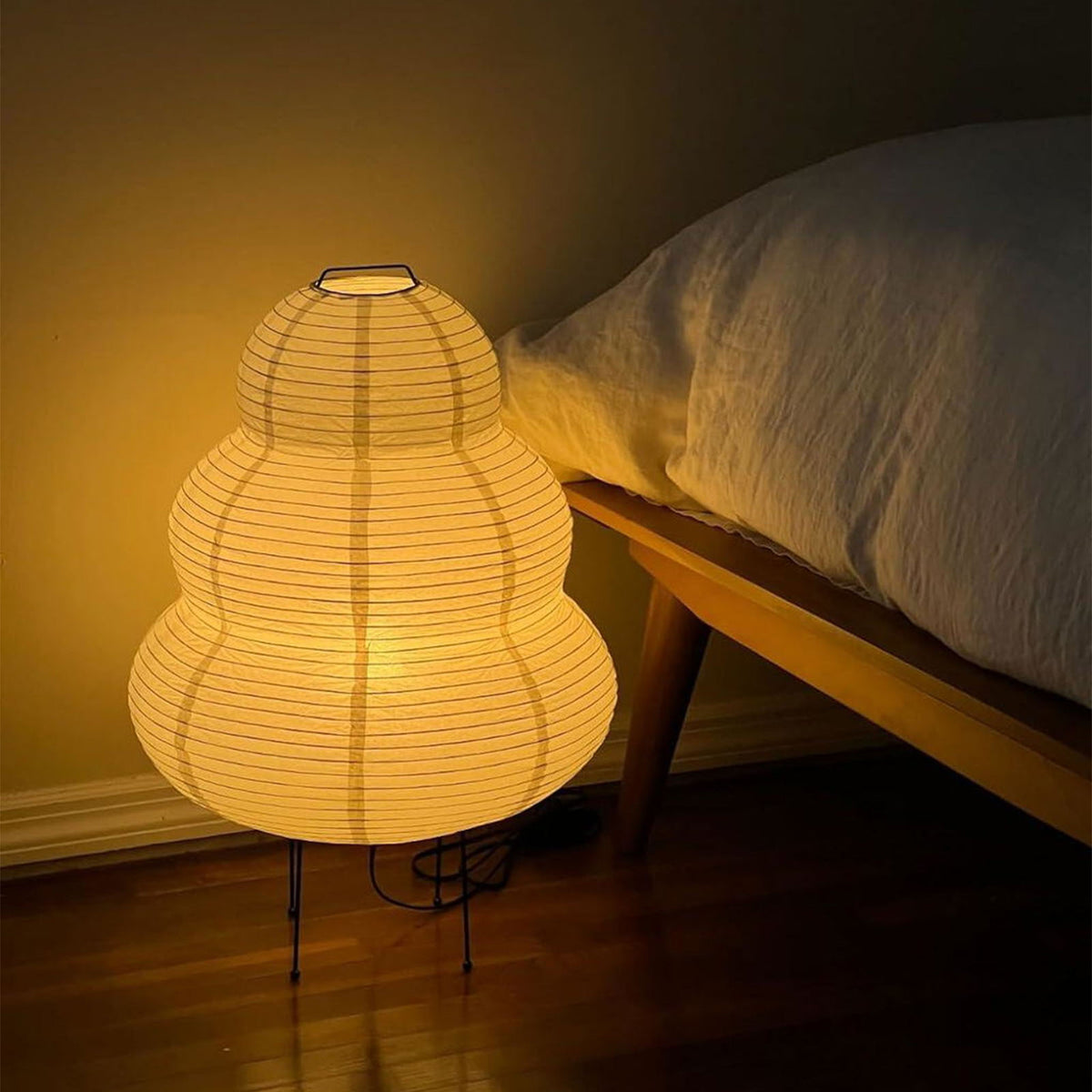 Nerine Tiered Washi Paper Table Lamp | Washi Paper and Metal | Glowing softly on the floor next to a bed in a dark room | Severn Lighting