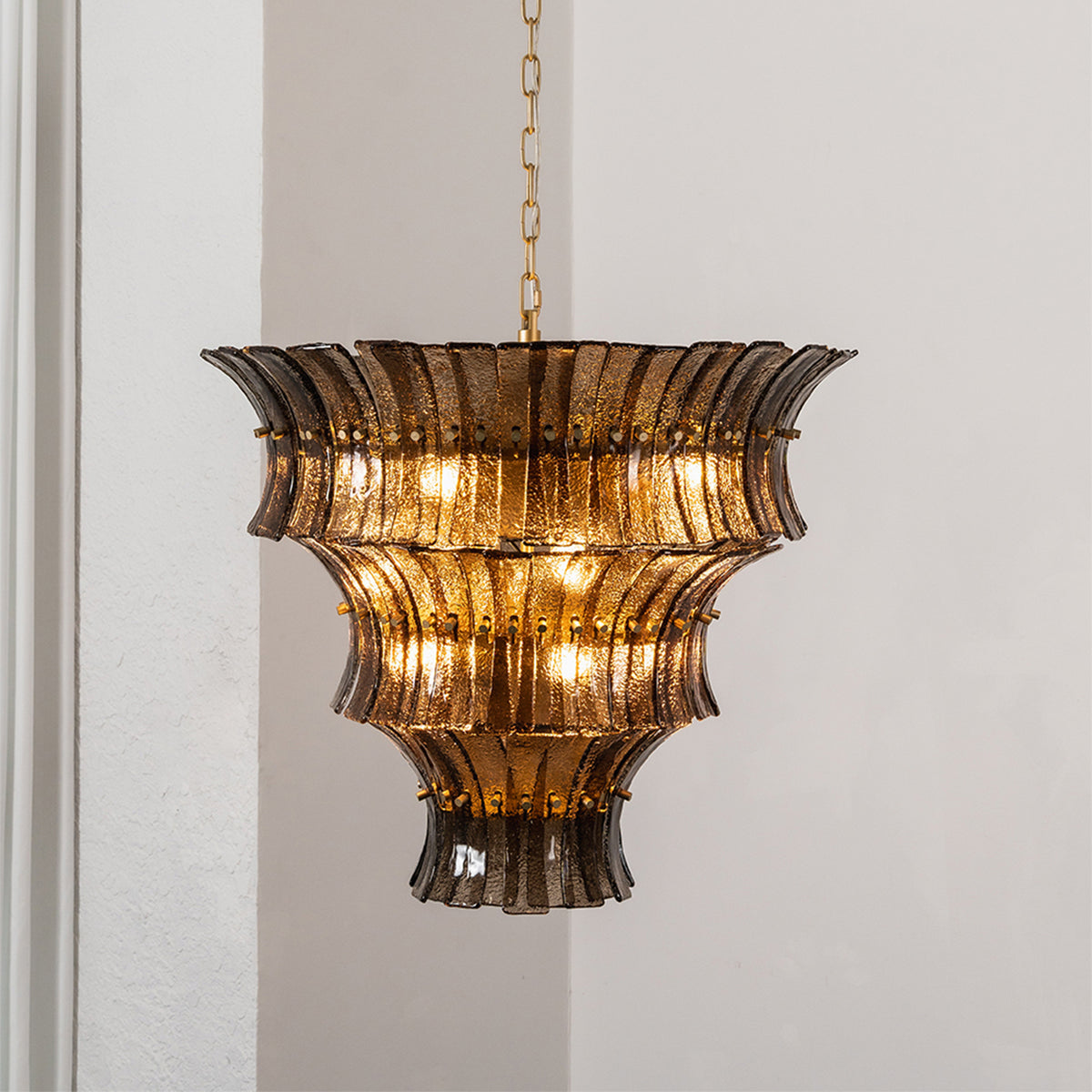 Octavia Sculptural Smoked Glass Chandelier | Textured Smoked Glass | Side view of the glowing multi-tiered chandelier positioned near a soft white curtain | Severn Lighting