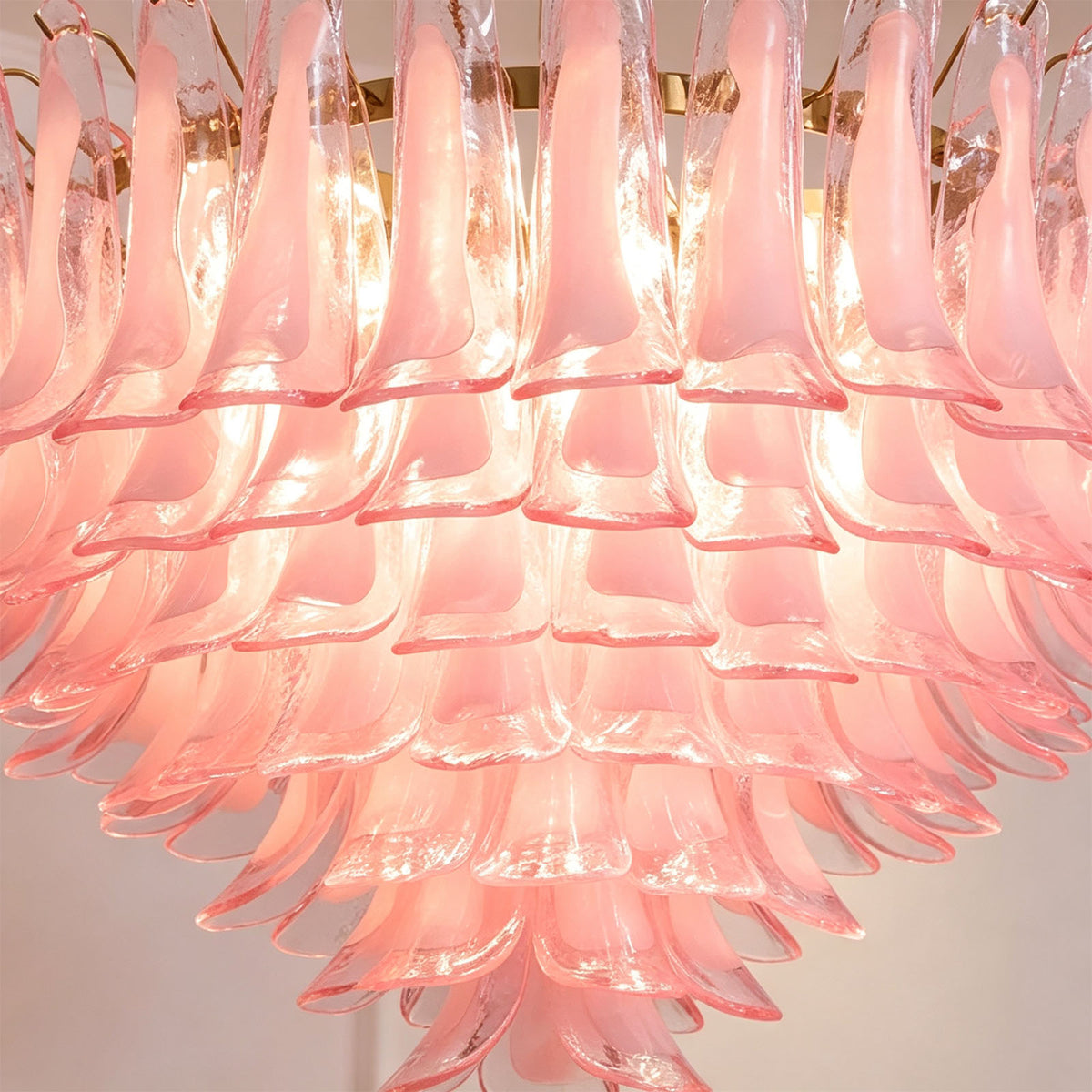 Ombeline Tiered Pink Glass Chandelier | Pink Glass and Brass | Full view of the glowing pink glass chandelier on a light wall backdrop | Severn Lighting