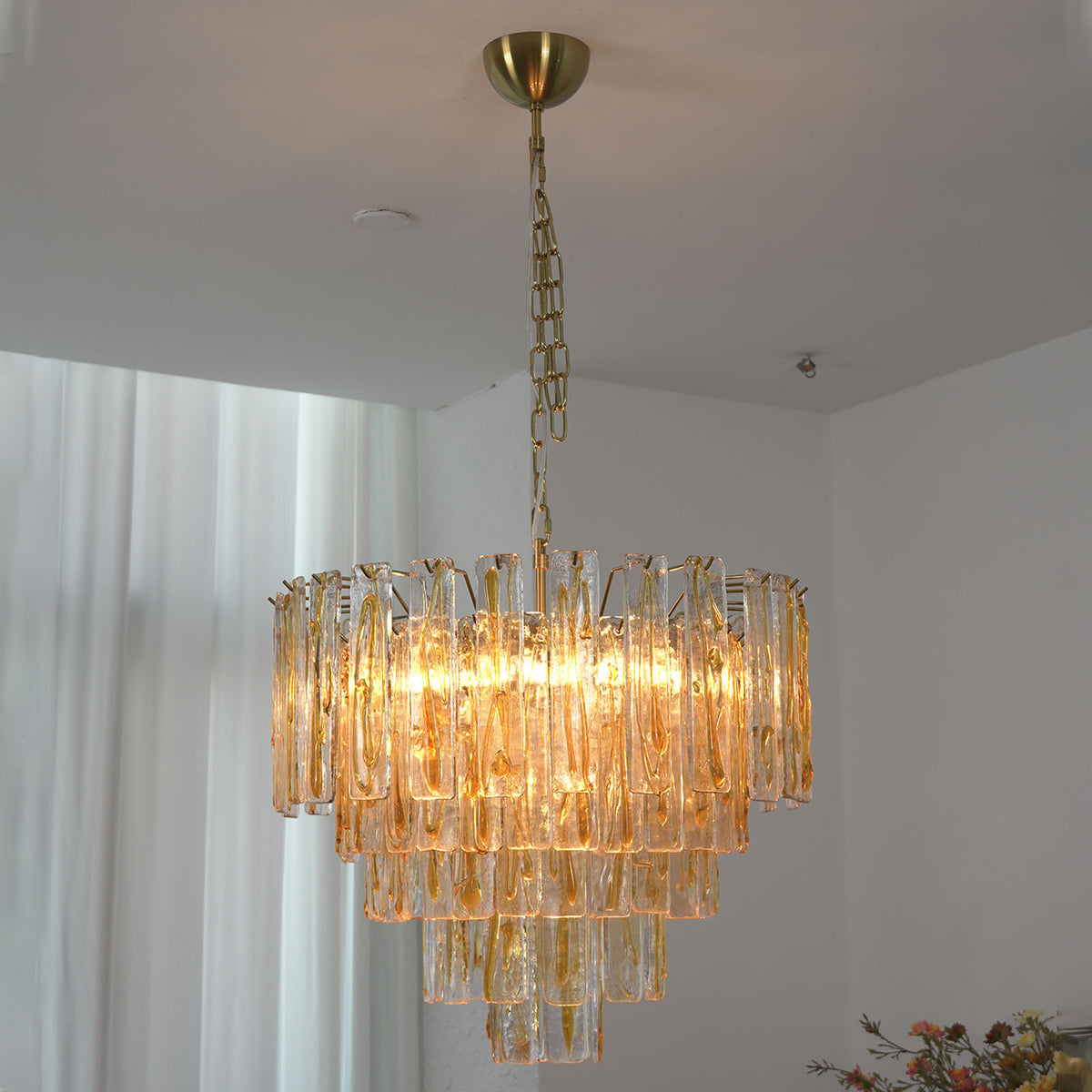 Orvelane Amber Swirl Glass Tiered Chandelier | Amber Swirl Glass and Brass | Real-life installation view glowing softly in a room near white window drapes | Severn Lighting