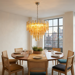 Orvelane Amber Swirl Glass Tiered Chandelier | Amber Swirl Glass and Brass | Styled above a round wooden dining table with woven chairs near large windows | Severn Lighting