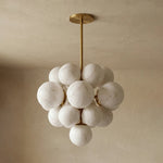 Ottoline Alabaster Cluster Chandelier | Natural Alabaster and Brass | Standard product display hanging against a textured beige backdrop with spheres subtly illuminated | Severn Lighting