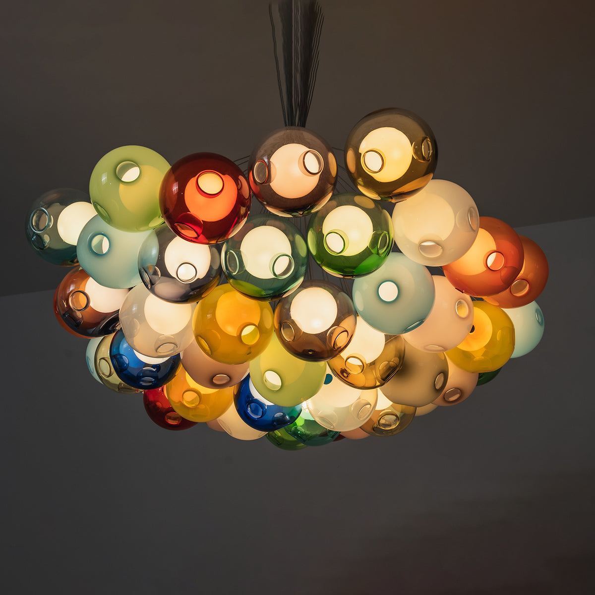 Rainbow Glass Bubble Cluster Chandelier | Multi-colored Blown Glass and Metal Cords | Looking up perspective of the glowing colorful glass cluster fixture against a dark background | Severn Lighting
