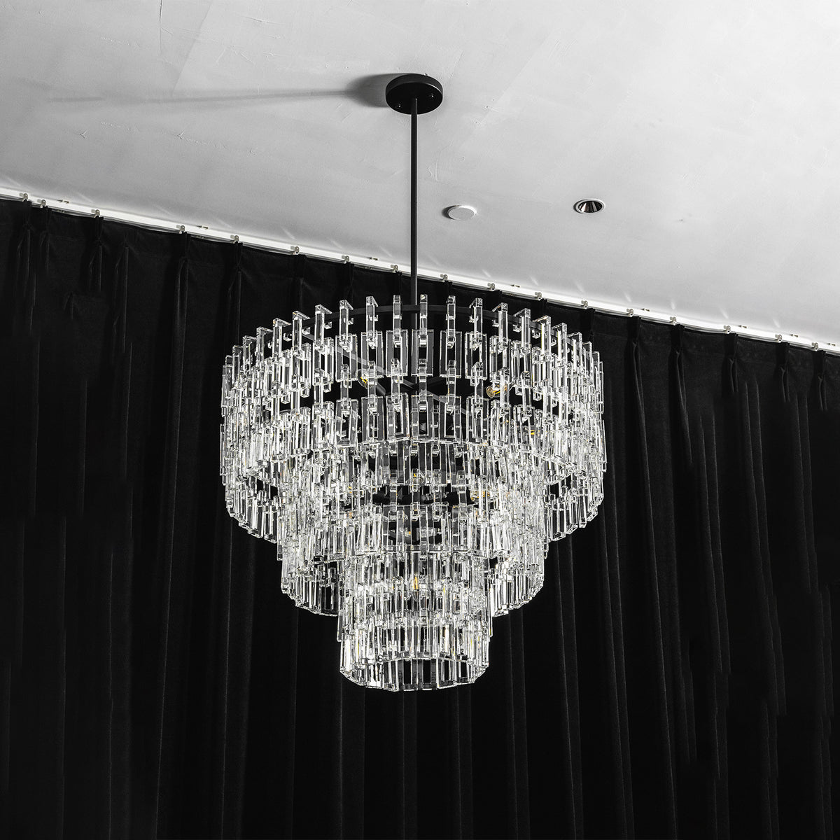 Rainer Cascading Glass Rod Chandelier | Clear Glass and Black Metal | Studio full shot of the chandelier illuminated against dark curtains | Severn Lighting