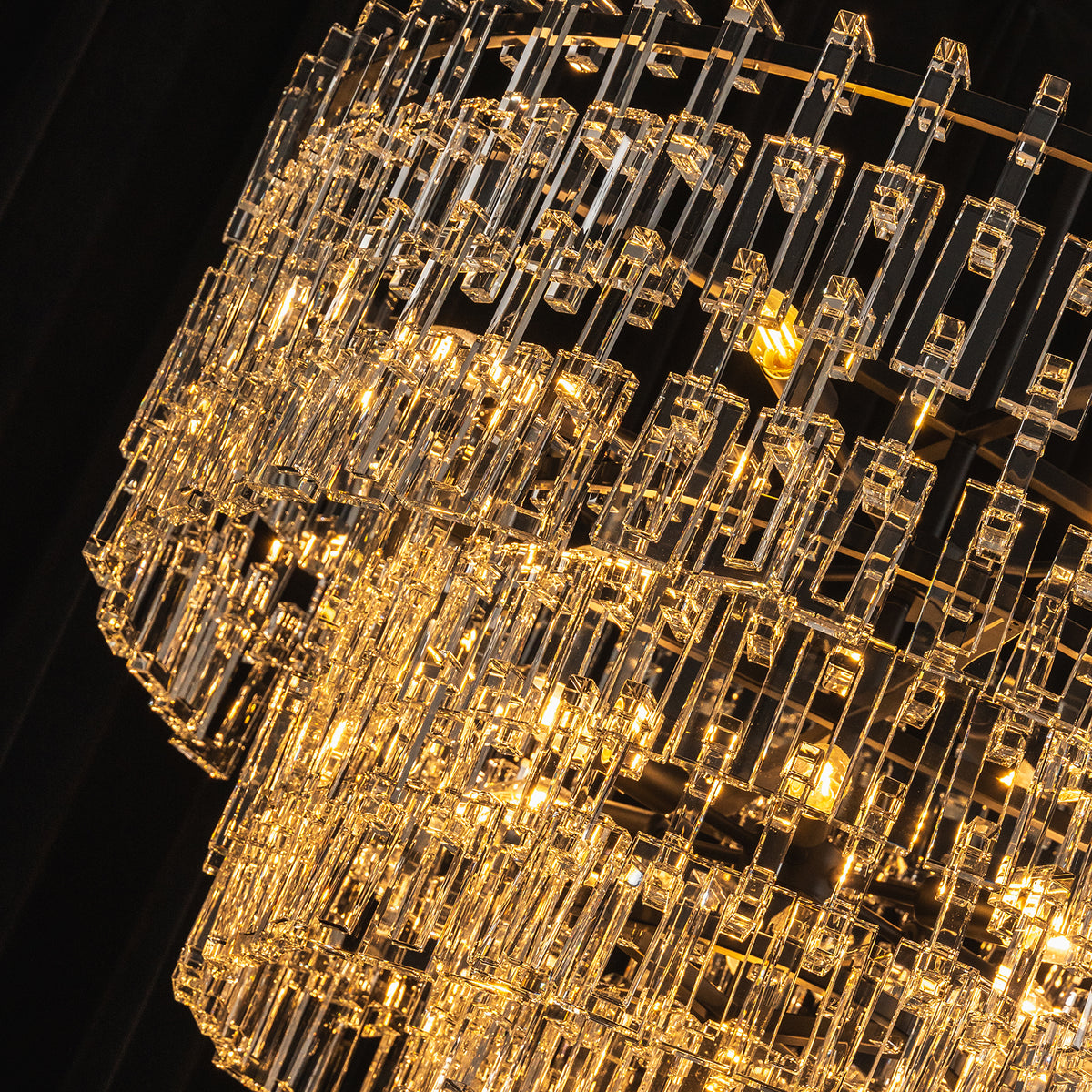 Rainer Cascading Glass Rod Chandelier | Clear Glass and Black Metal | Angle close-up view highlighting the glowing multi-tiered glass rods | Severn Lighting