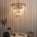 Rainer Cascading Glass Rod Chandelier | Clear Glass and Black Metal | Ambient lighting shot hanging against vertical fluted wall panel | Severn Lighting
