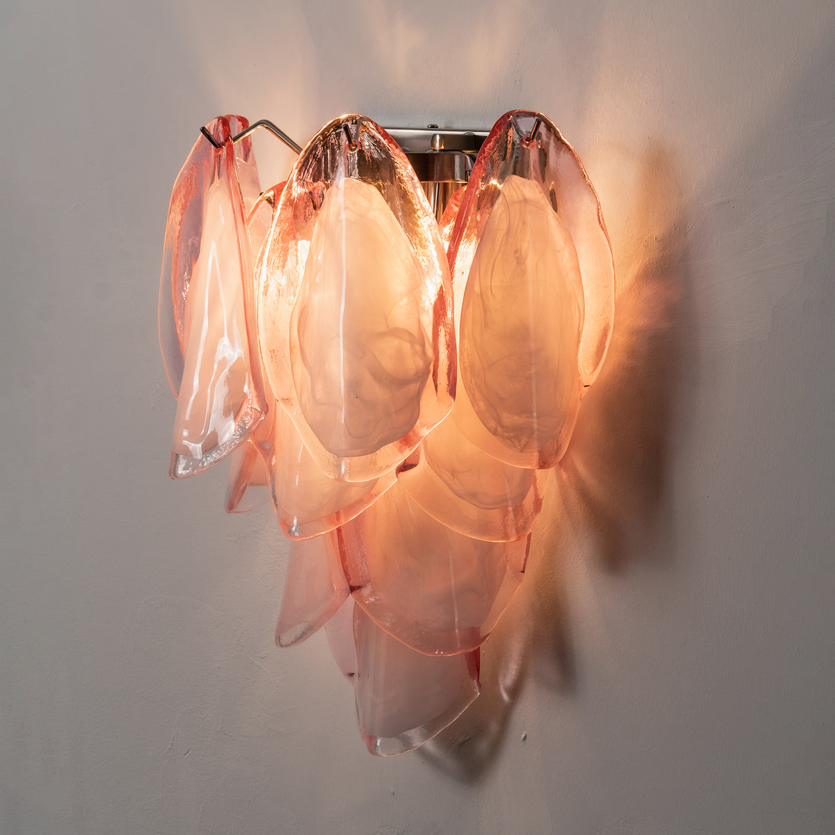 Rosalind Rose Glass Wall Sconce | Glass, Metal | Staged close-up view of the fully lit pink petal sconce throwing a dramatic warm golden-pink ambient light halo on a dark background | Severn Lighting