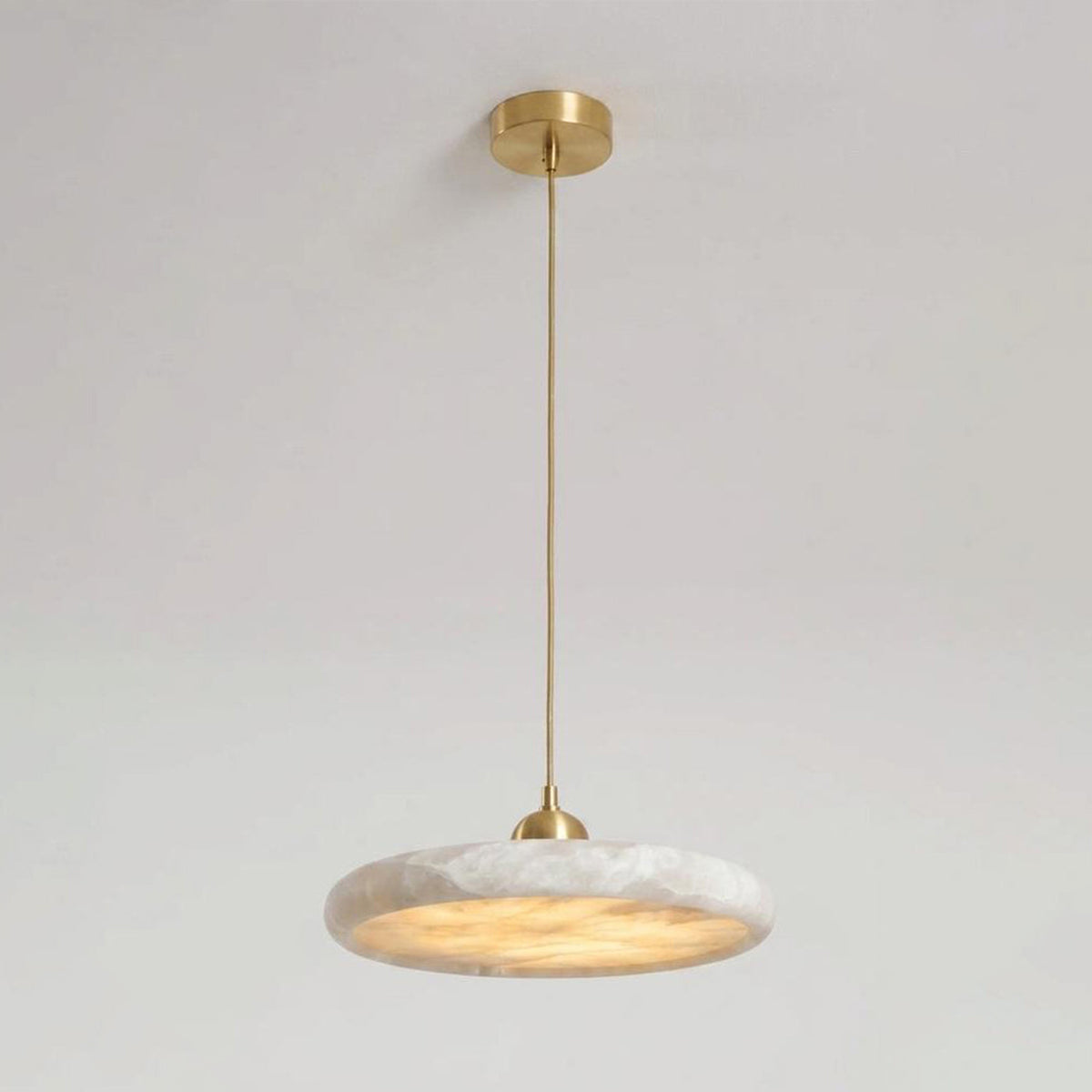 Sabine Alabaster Disc Pendant Light | Natural Alabaster and Brass | Medium close-up glowing softly against a bright window backdrop | Severn Lighting