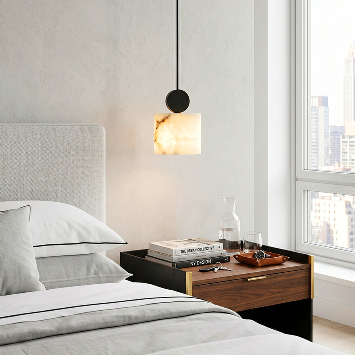 Sabine Alabaster Drum Pendant Light | Natural Alabaster and Brass | Stylized bedtime reading lamp hovering above a wooden nightstand in a bright minimalist bedroom | Severn Lighting