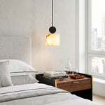 Sabine Alabaster Drum Pendant Light | Natural Alabaster and Brass | Stylized bedtime reading lamp hovering above a wooden nightstand in a bright minimalist bedroom | Severn Lighting