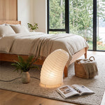 Severine Spiral Washi Paper Table Lamp | Washi Paper and Metal | Styled on the floor beside a cozy bed in a modern bedroom | Severn Lighting