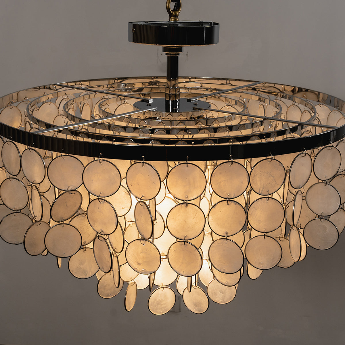 Sirena Capiz Disc Tiered Ceiling Light | Shell, Metal | Front view of the fully lit ceiling light against a dark grey background, highlighting the golden translucency | Samu Lamp