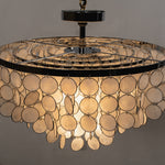 Sirena Capiz Disc Tiered Ceiling Light | Shell, Metal | Front view of the fully lit ceiling light against a dark grey background, highlighting the golden translucency | Samu Lamp