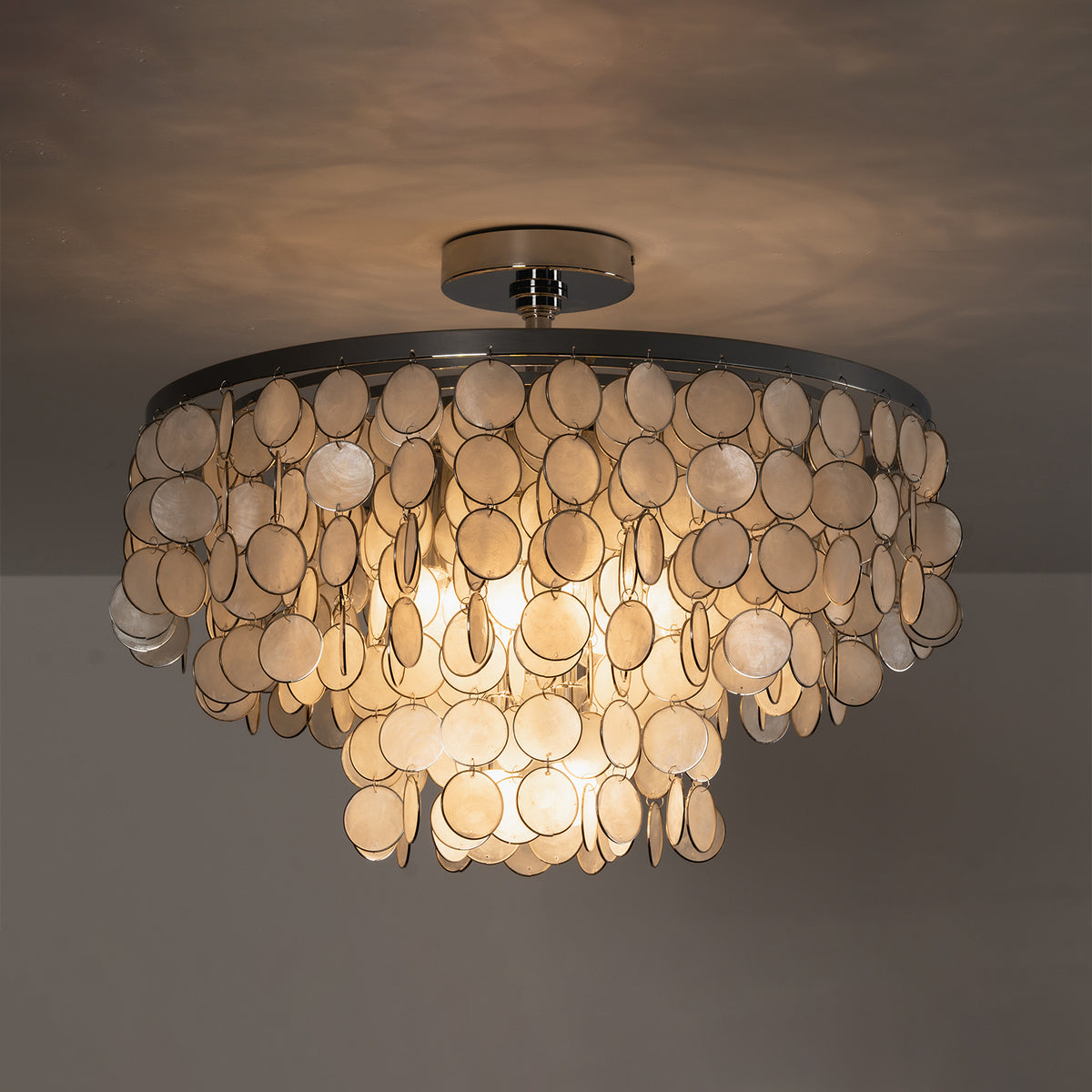 Sirena Capiz Disc Tiered Ceiling Light | Shell, Metal | Full view of the tiered shell chandelier lit up brilliantly against a moody dark studio background | Isolated shot | Samu Lamp