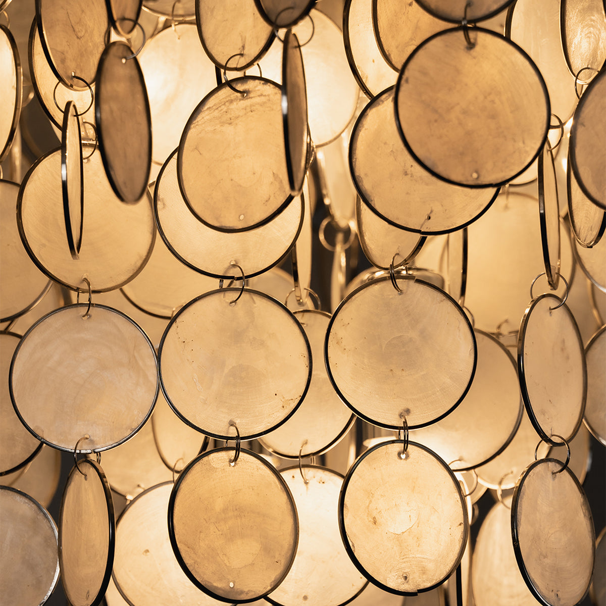 Sirena Capiz Disc Tiered Ceiling Light | Shell, Metal | Macro focus on the translucent circular capiz shells glowing with warm yellow backlighting | Detail shot | Samu Lamp