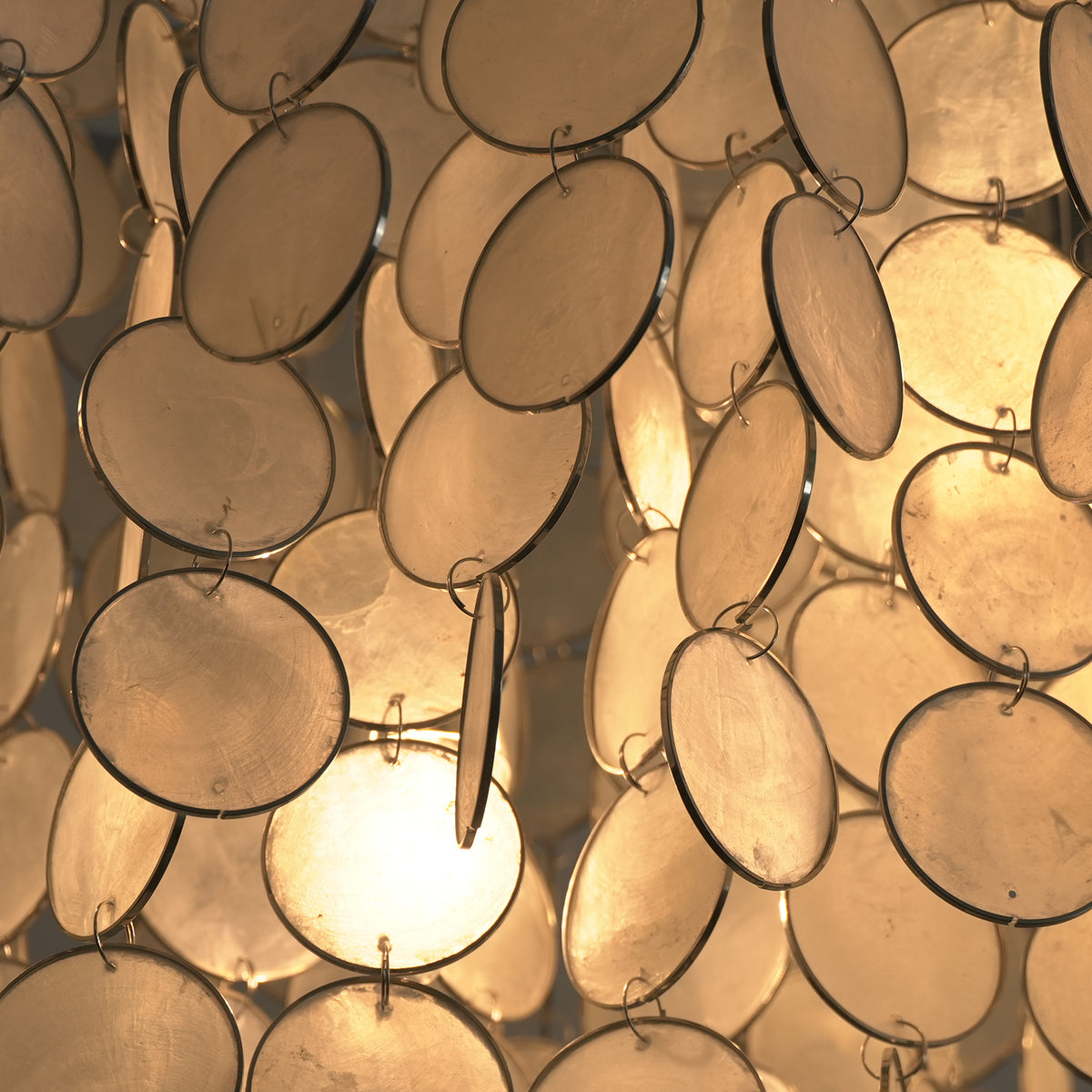Sirena Capiz Elongated Linear Chandelier | Capiz Shell, Metal | Close-up macro view of the translucent capiz shell discs radiating a brilliant, warm internal light | Detail shot | Samu Lamp