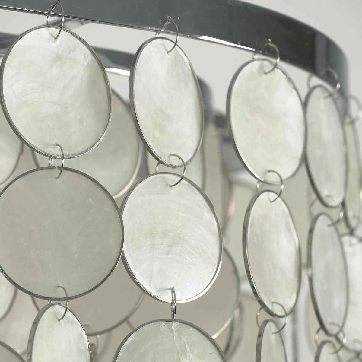 Sirena Capiz Elongated Linear Chandelier | Capiz Shell, Metal | Close-up view of the unlit pearlescent capiz shell circles attached to a shiny chrome metal framework | Detail shot | Samu Lamp