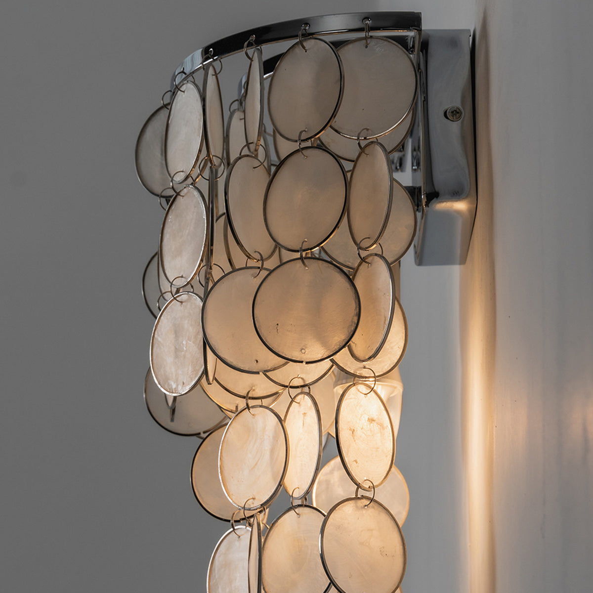 Sirena Capiz Tiered Wall Sconce | Capiz Shell, Metal | Side profile view of the illuminated wall sconce showcasing its layered depth and warm backlight projection on a wall | Samu Lamp