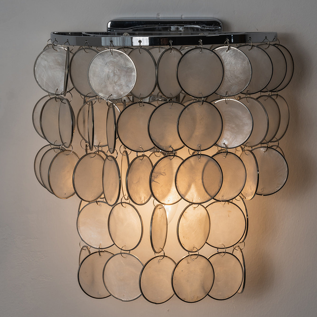 Sirena Capiz Tiered Wall Sconce | Capiz Shell, Metal | Front view of the fully lit cascading shell wall sconce radiating a warm golden glow against a neutral studio background | Samu Lamp
