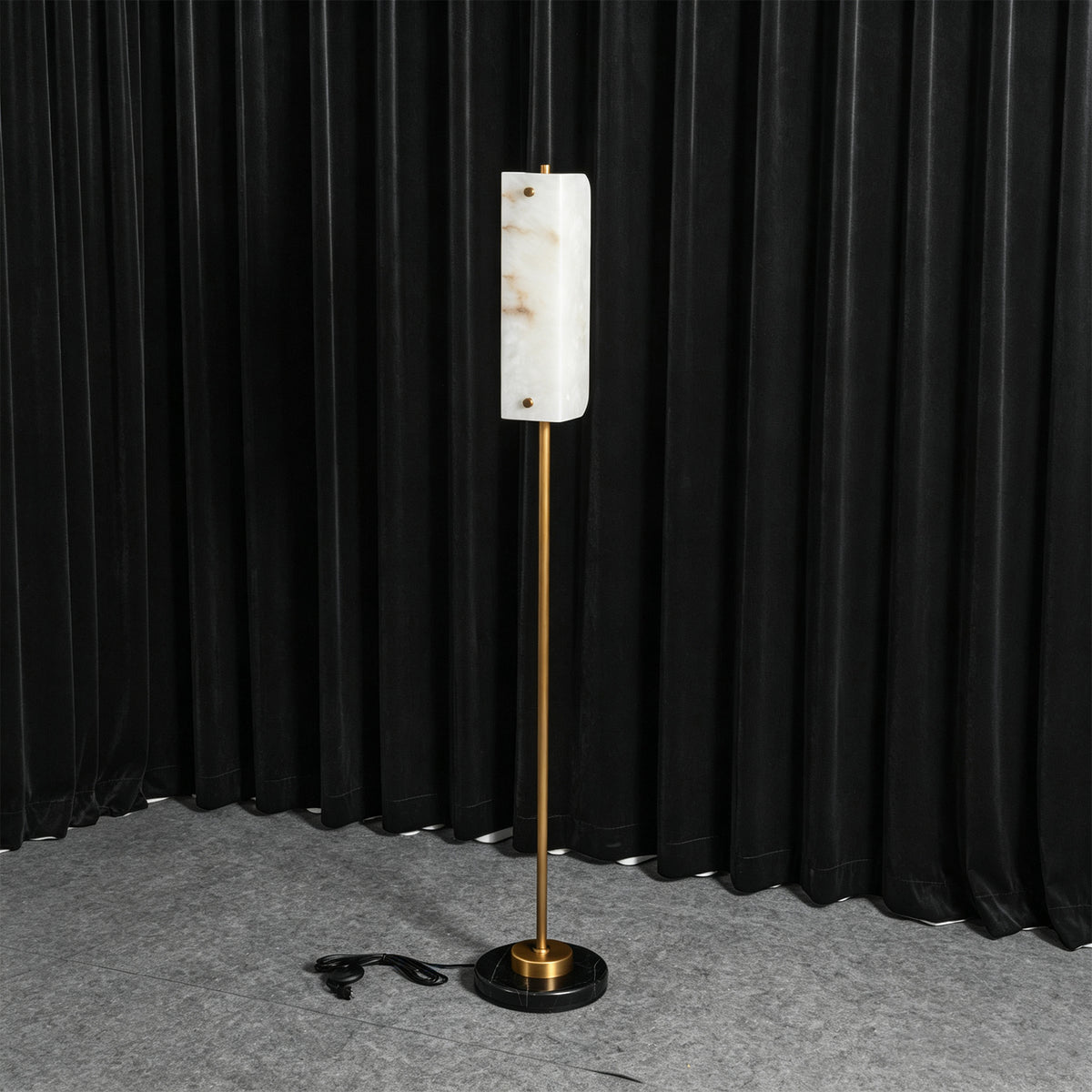 Stellan Alabaster Column Floor Lamp | Natural Alabaster, Brass and Black Metal | Illuminated full view displayed against a dark curtain backdrop | Severn Lighting