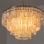 Thalassa Tiered Capiz Shell Chandelier | Capiz Shell, Metal | Angular close-up of the fully illuminated tiered chandelier radiating an intense, warm golden ambient glow from within the shell layers | Severn Lighting