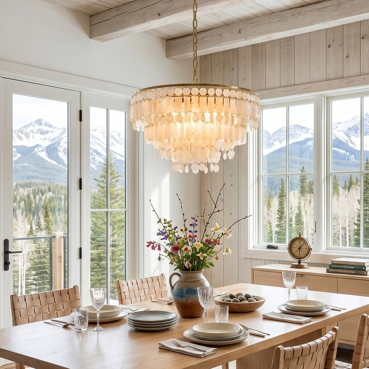 Thalassa Tiered Capiz Shell Chandelier | Capiz Shell, Metal | Hanging as a grand coastal centerpiece over a wooden dining table in a bright room with large windows overlooking snowy mountains | Severn Lighting