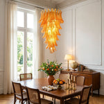 Thessaly Amber Glass Plume Chandelier | Amber Glass and Brass | Suspended over a wooden dining table in a bright room | Severn Lighting