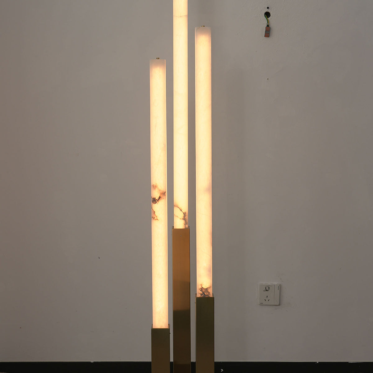 Trelune Column Floor Lamp | Alabaster and Brass | Three tiered columns illuminated against white room wall | Severn Lighting