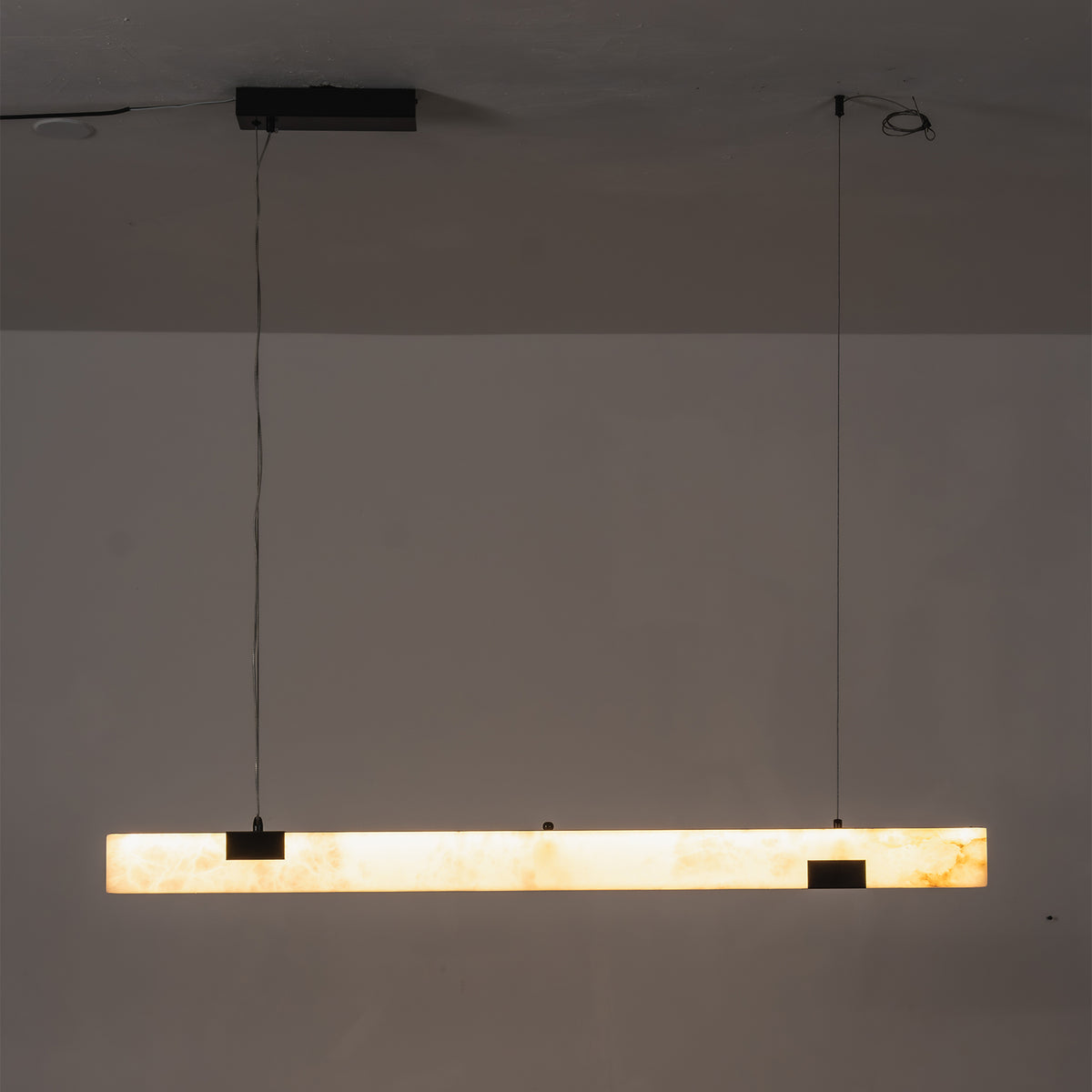 Vale Alabaster Linear Glow Pendant Lighting | Natural Alabaster and Black Metal | Horizontal studio view of the linear alabaster fixture fully lit against a dark background | Severn Lighting
