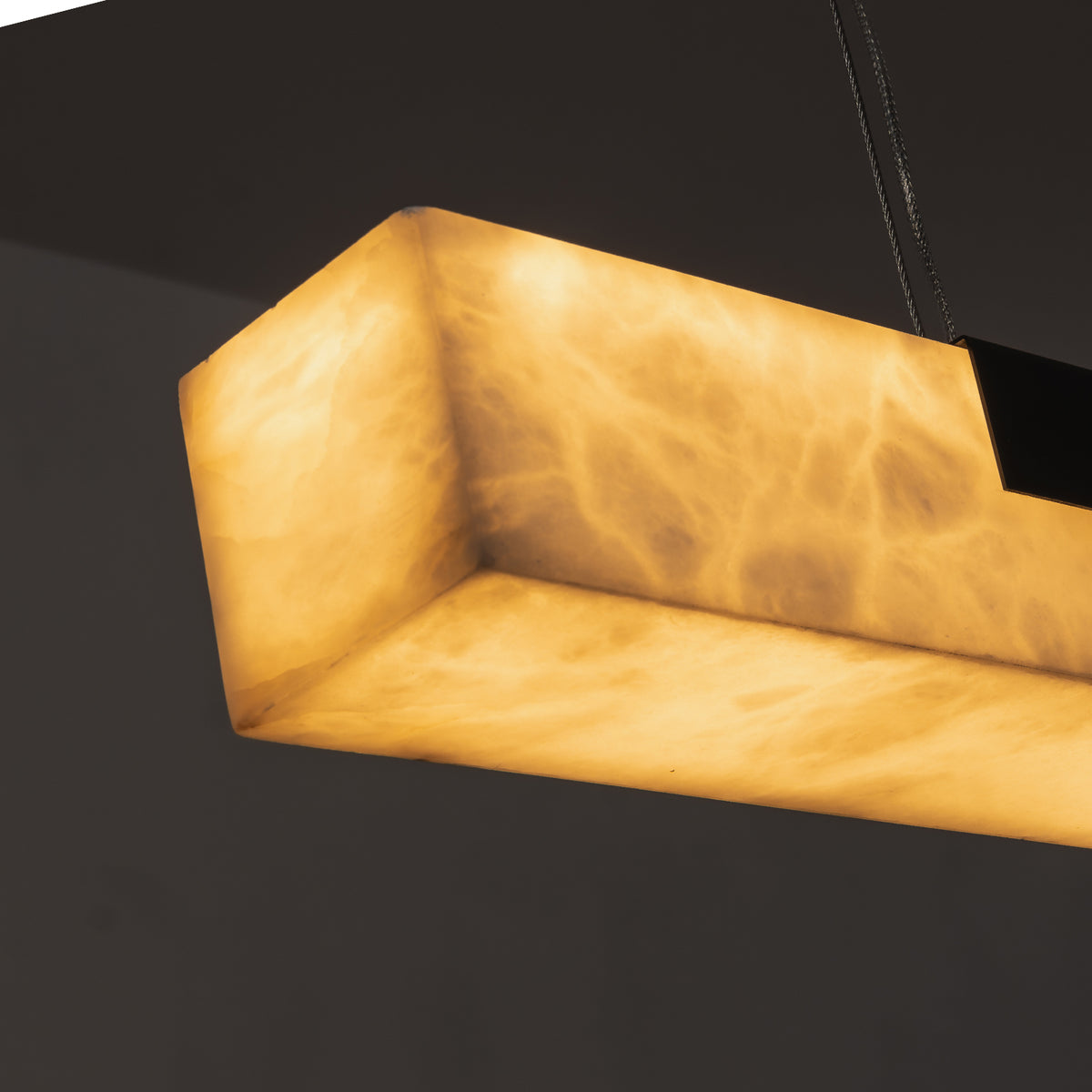 Vale Alabaster Linear Glow Pendant Lighting | Natural Alabaster and Black Metal | Perspective close-up view looking up at the illuminated bottom of the linear stone shade | Severn Lighting