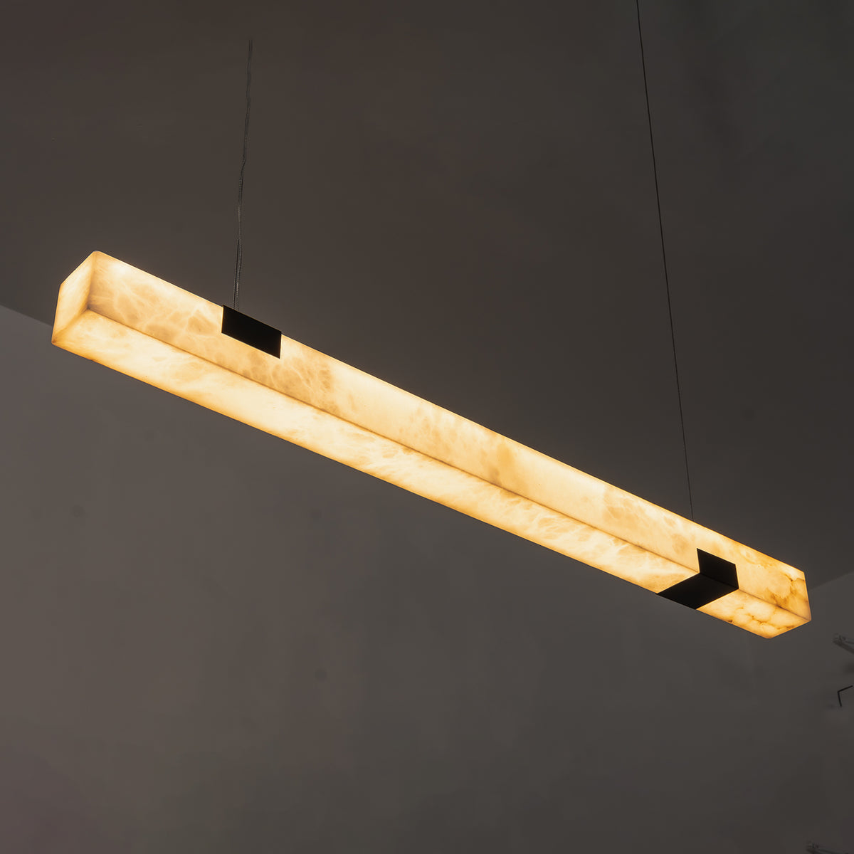 Vale Alabaster Linear Glow Pendant Lighting | Natural Alabaster and Black Metal | Angled studio display of the lit linear alabaster pendant fixture against a dark wall | Severn Lighting