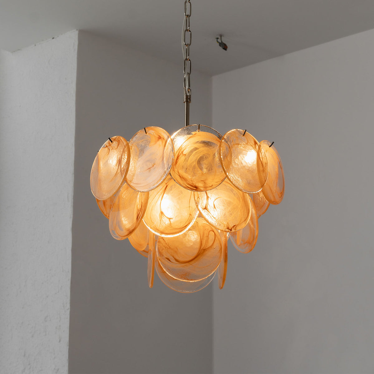Vaucelle Swirled Glass Disc Tiered Chandelier | Swirled Glass and Brass | Yellow amber glass variant hanging illuminated in a room corner | Severn Lighting