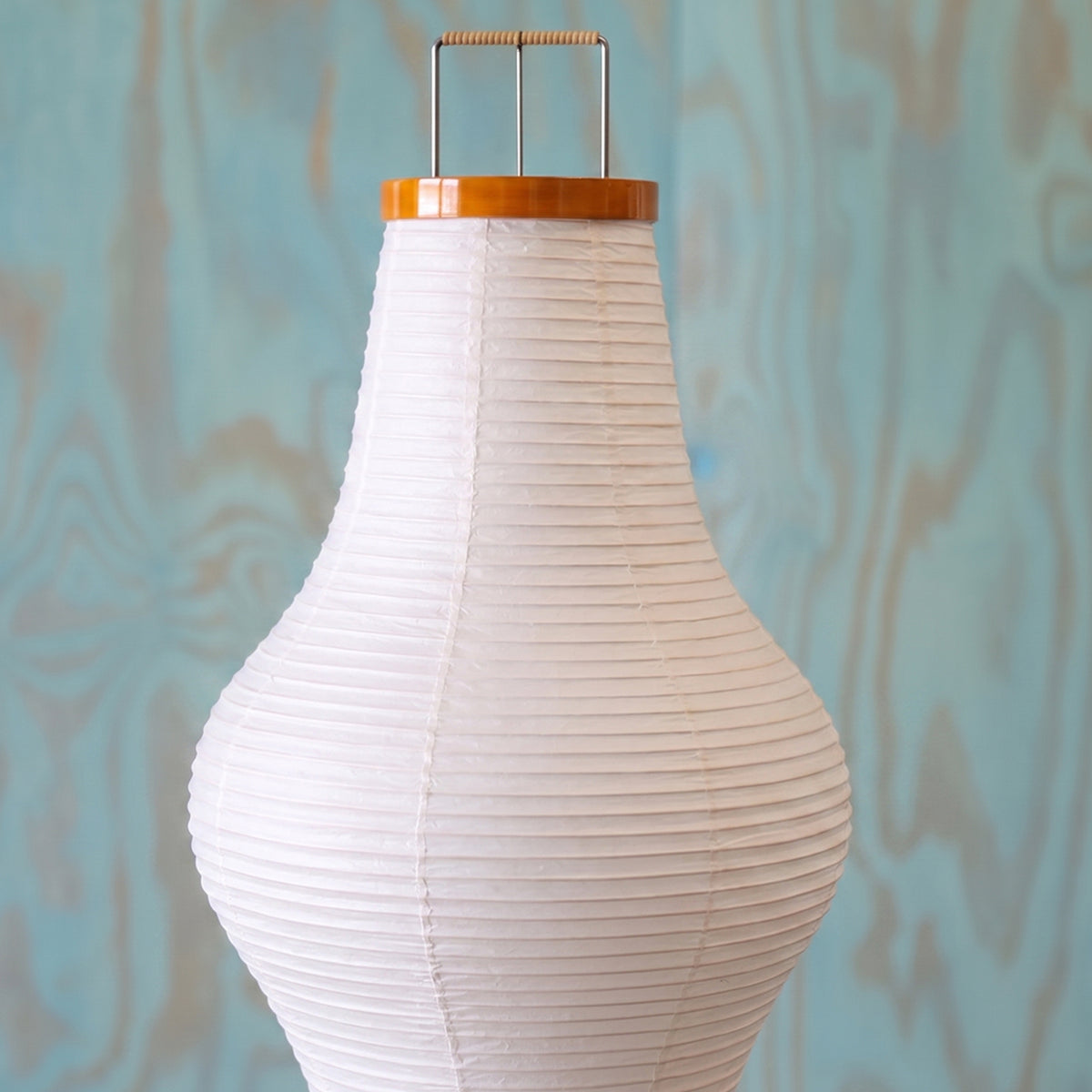 Verena Ribbed Paper Column Floor Lamp | Ribbed Paper and Metal Tripod Legs | Macro view of the white sculptural paper shade upper silhouette against a textured blue background | Severn Lighting