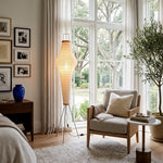 Verena Ribbed Paper Column Floor Lamp | Ribbed Paper and Metal Tripod Legs | Positioned in a cozy living room corner next to a comfortable cream armchair and a gallery wall | Severn Lighting