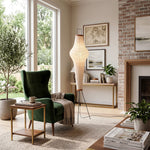 Verena Ribbed Paper Column Floor Lamp | Ribbed Paper and Metal Tripod Legs | Styling a bright living space beside a luxurious green velvet armchair and a wooden fireplace mantel | Severn Lighting