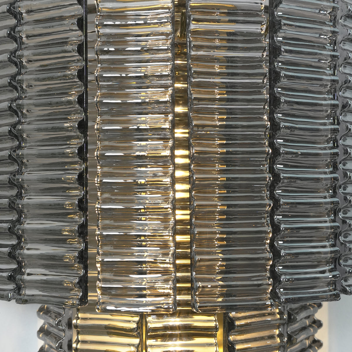 Vespera Tiered Smoky Glass Wall Lamp | Glass, Metal | Macro close-up focus on the densely packed vertical smoky glass ribs radiating a warm amber light from within | Detail shot | Severn Lighting