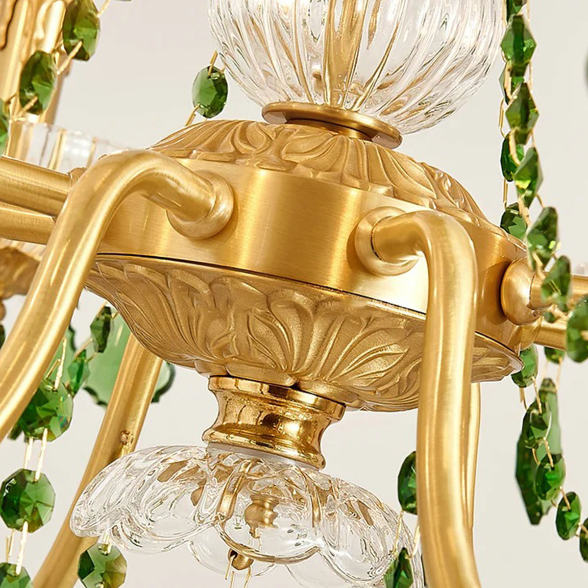 Vionne Green Crystal Drop Brass Chandelier | Green Crystal, Clear Glass and Brass | Macro shot of the ornate brass center bowl where the scrolling arms connect | Severn Lighting